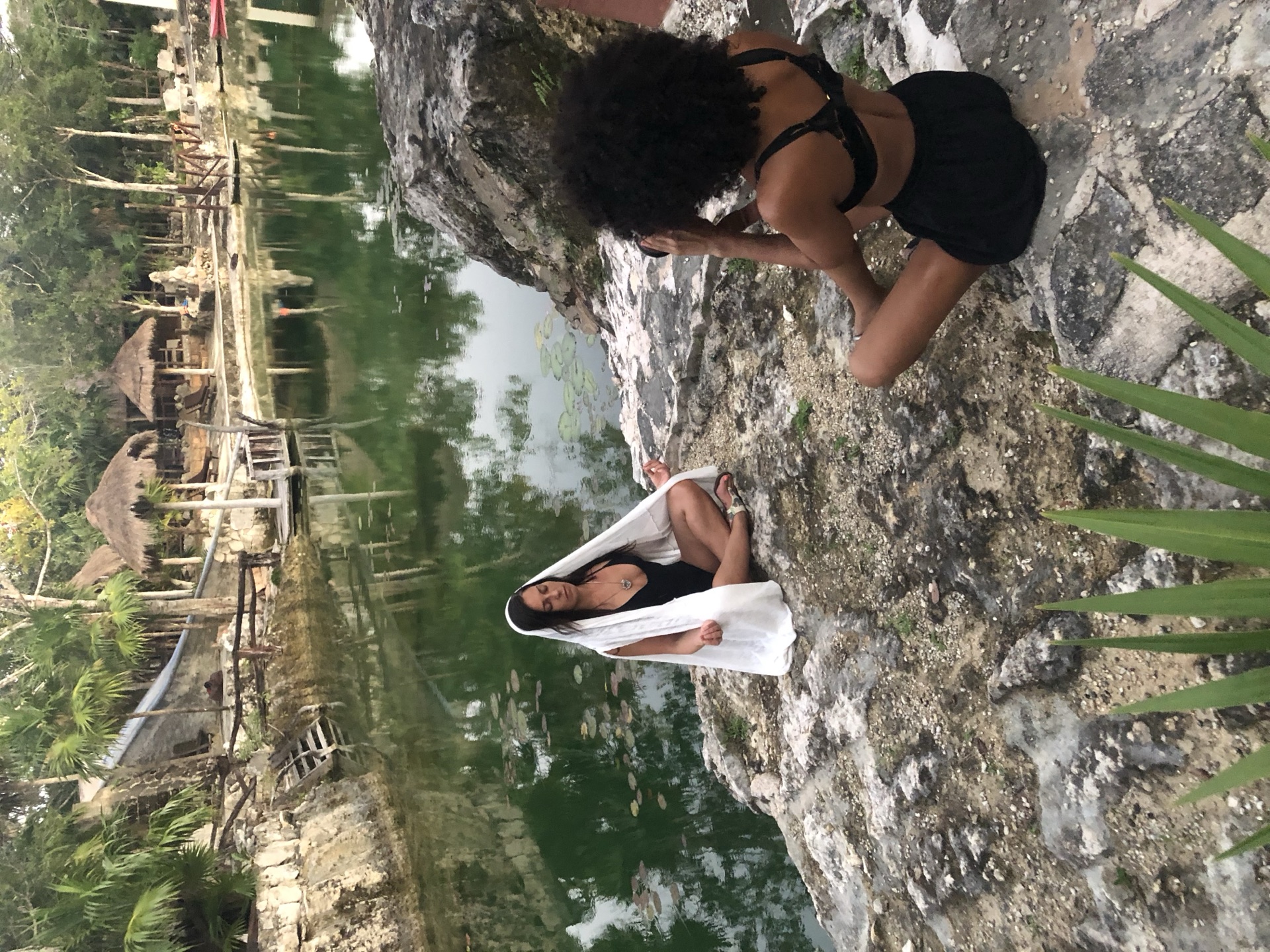 Two people meditating beside a pool among trees