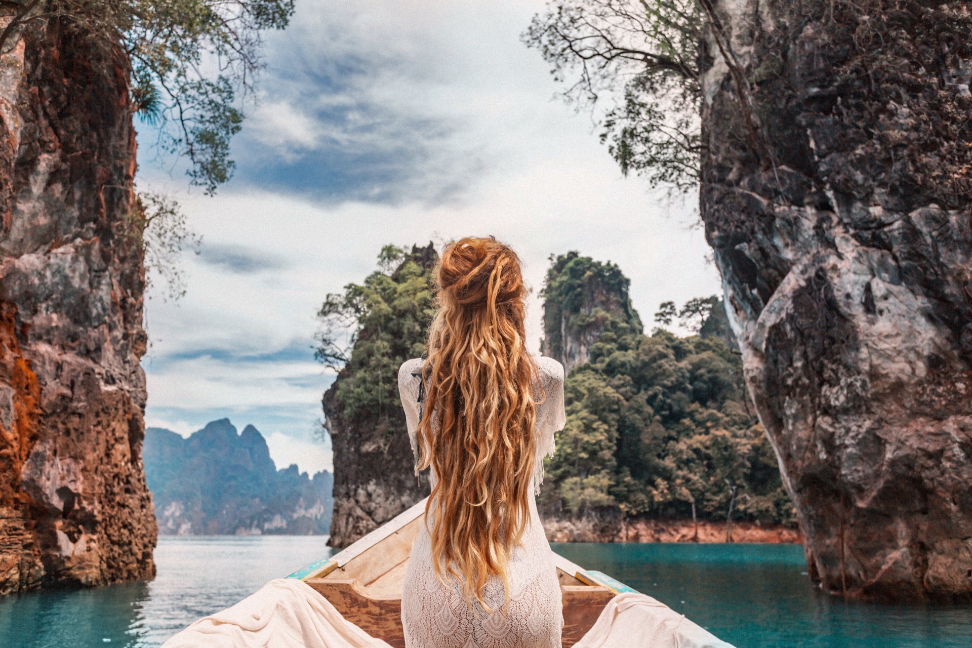 A traveler looking toward limestone cliffs and turquoise water from a wooden boat